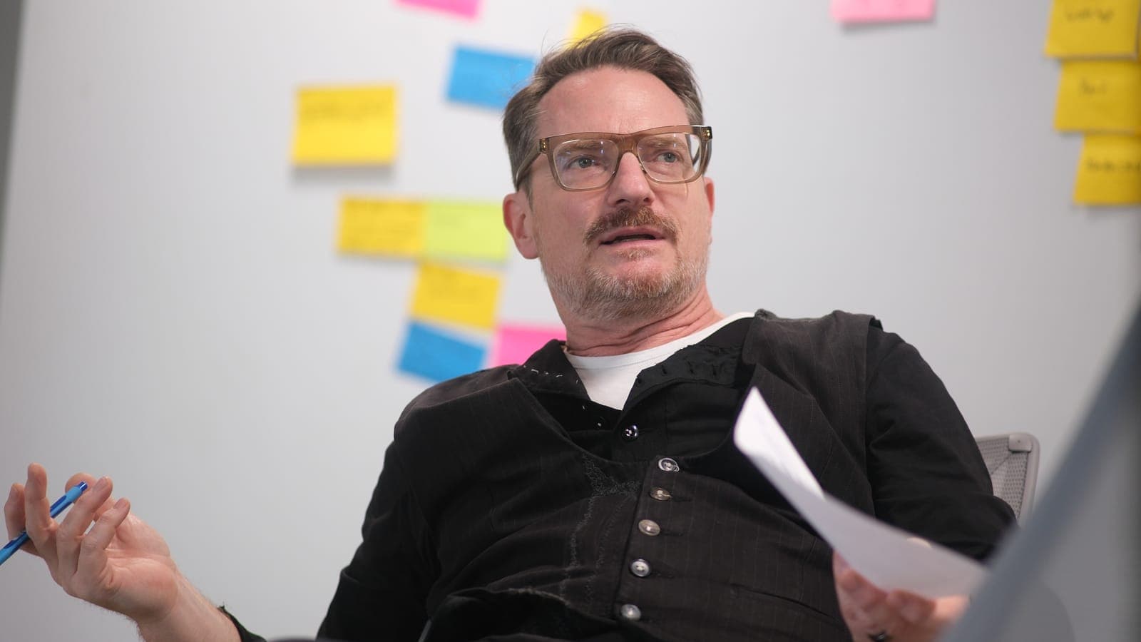 Manuel Kreutz mit Stift und einem Blatt Papier in den Händen vor einer Wand mit bunten Haftnotizen